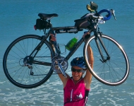 Lynn West Salvo ’71 hoists her bike over her head on the beach